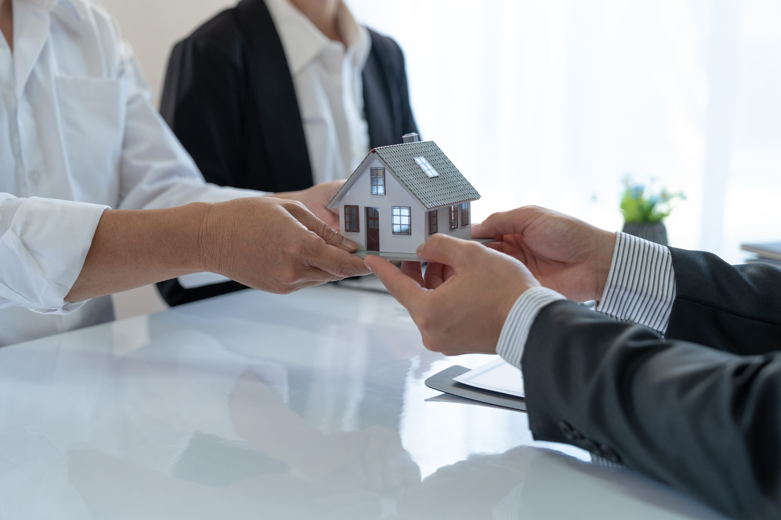 Young Asian real estate agent, and insurance salesman handing over a sample house to a client after signing the sale at the office.